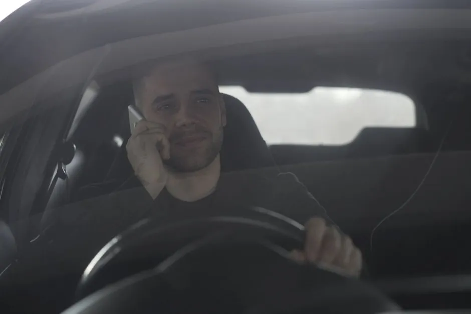 Conducteur tenant son téléphone au volant, main sur l'écran, circulation urbaine vue de l'intérieur